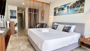 A modern hotel room with a large bed, a desk, and a painting of a coastal scene.