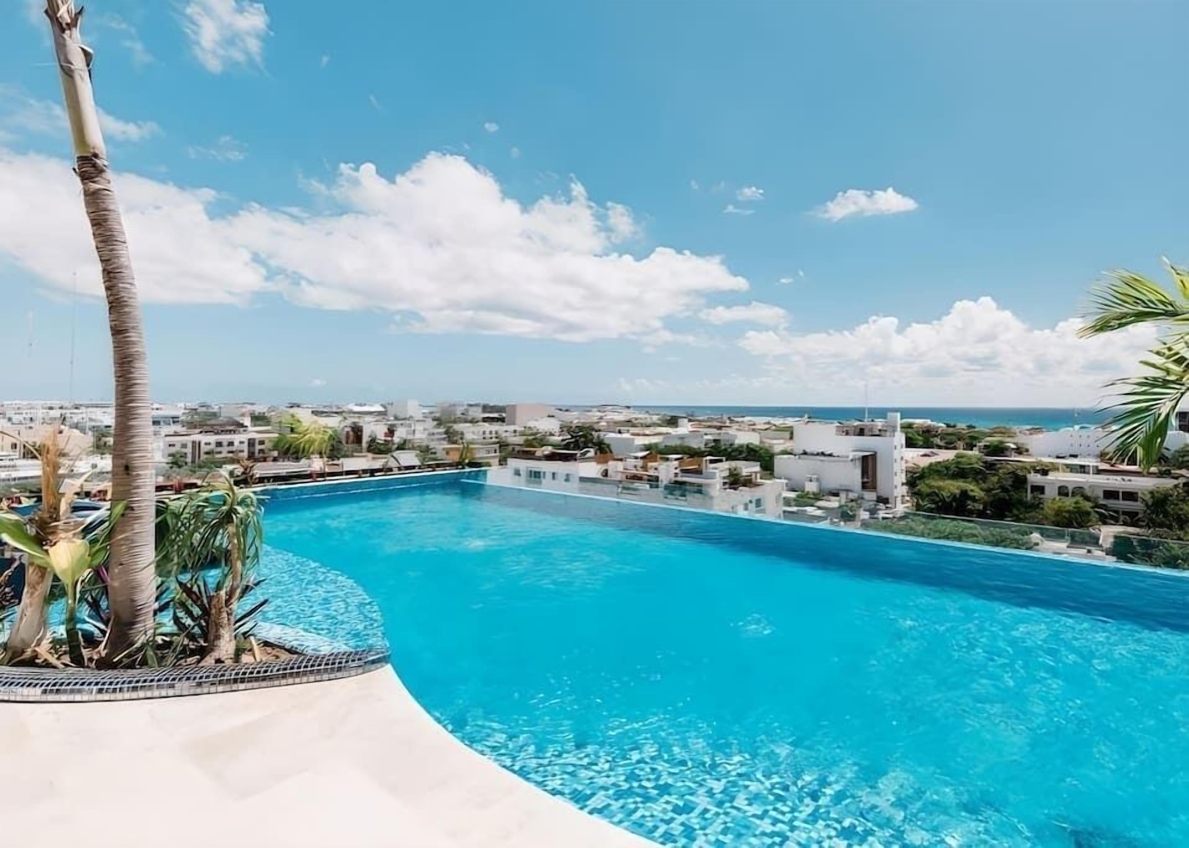 Une piscine offrant une vue sur une ville côtière et des palmiers.
