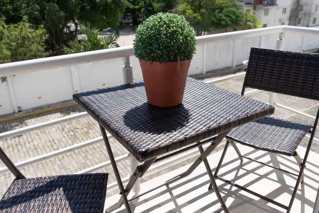 Ein Balkon mit einem kleinen Tisch, zwei Stühlen, einem Blumentopf und Blick auf eine Straße und Gebäude.