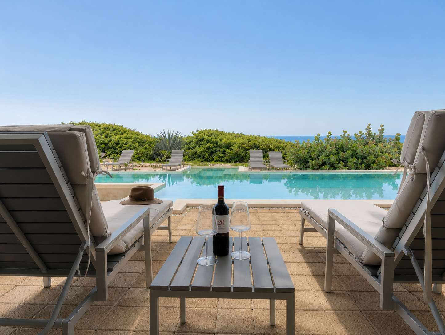 Ein Poolbereich mit Liegestühlen, einem Tisch mit Flasche und Glas sowie Blick auf den Ozean.