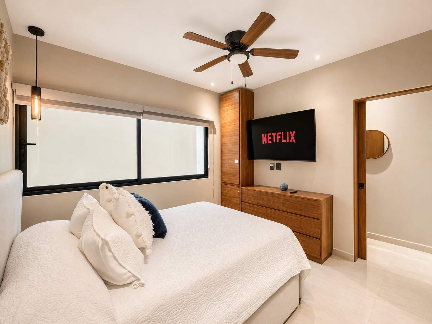 A bedroom with a bed, a ceiling fan, a TV displaying 'NETFLIX,' a window, and a wooden dresser.