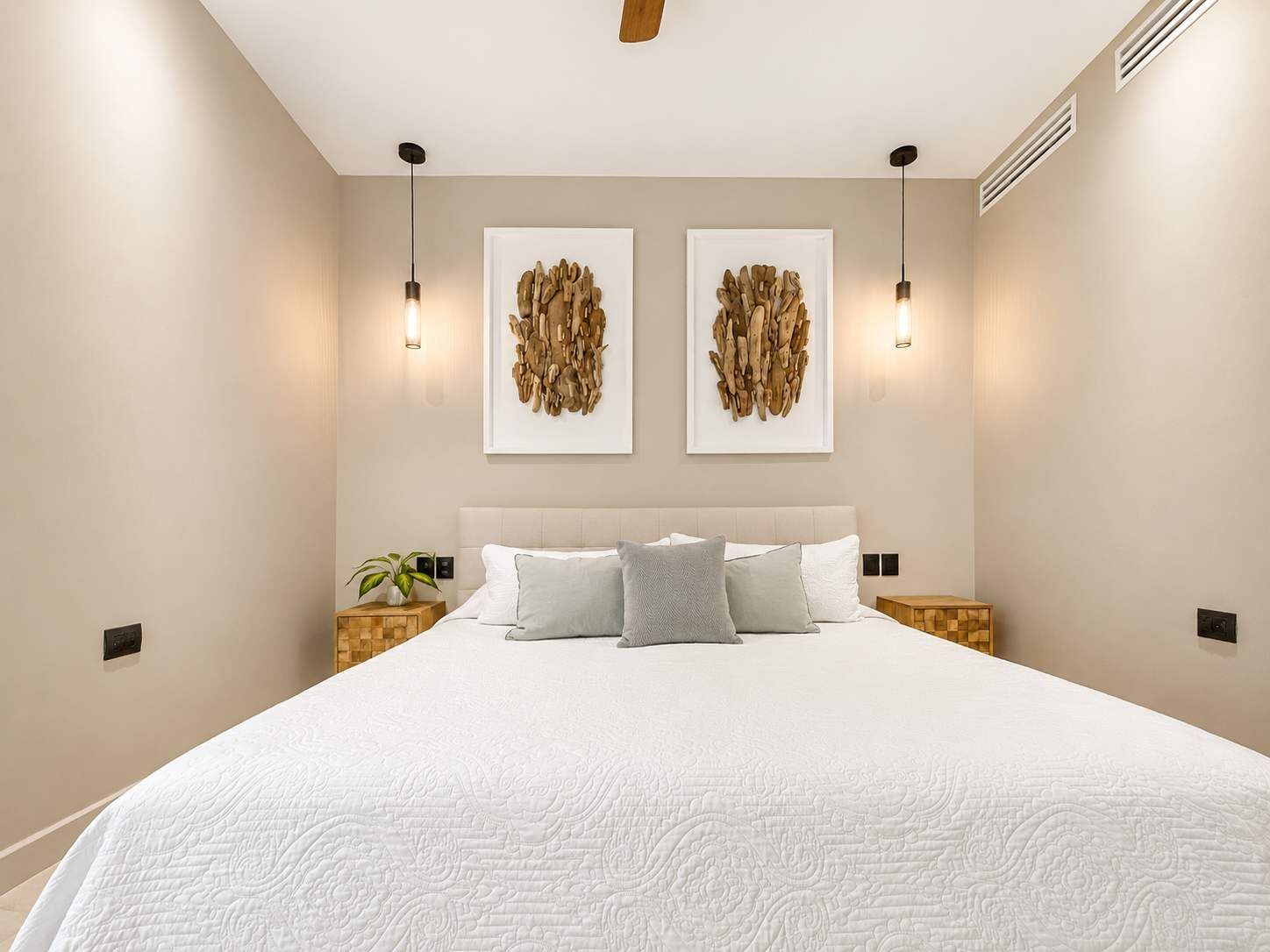 Une chambre à coucher avec un grand lit, deux appliques murales et deux œuvres d’art encadrées accrochées au mur.