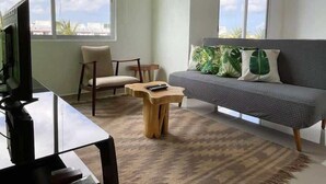 Una sala de estar con sofá, sillón, mesa de centro, televisor y ventanas amplias con vistas.