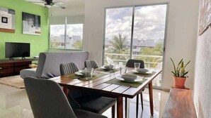 Un comedor con una mesa dispuesta para cuatro personas, un televisor y vistas de la ciudad a través de amplias ventanas.