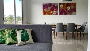 Una sala moderna con un sofá gris, una mesa de comedor con sillas y dos cuadros abstractos en la pared.