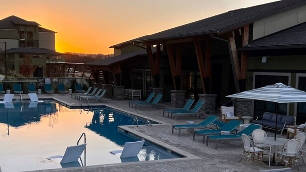 Zona de piscina con sillones y sombrillas, rodeada de edificios.
