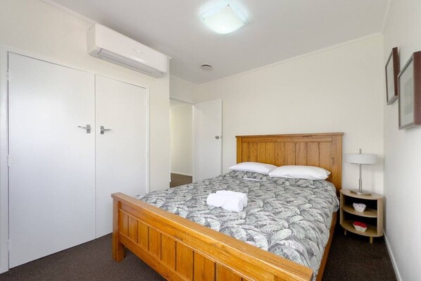 A bedroom with a wooden bed, a nightstand with a lamp, a wardrobe, and a ceiling light.