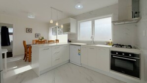 Une cuisine moderne avec des armoires blanches, un four encastré, une cuisinière à gaz et des luminaires suspendus.