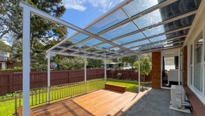 Un patio couvert doté d’une terrasse en bois, d’un banc et d’une structure vitrée.