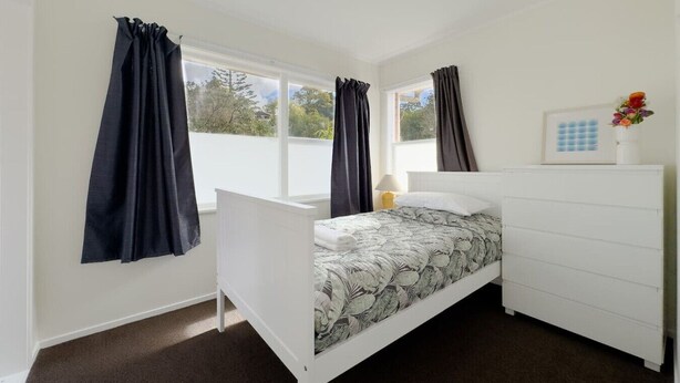 Une chambre avec un lit simple, une commode blanche et une fenêtre avec des rideaux.