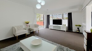 Un salon moderne avec un canapé blanc, une petite table, un téléviseur à écran plat et une grande fenêtre.