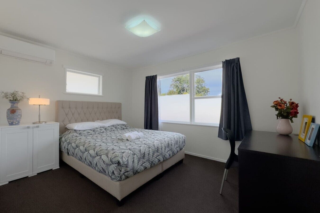 A bedroom with a bed, a bedside table with a lamp, a window with curtains, and a view of the outside.