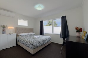 A bedroom with a bed, a bedside table with a lamp, a window with curtains, and a view of the outside.