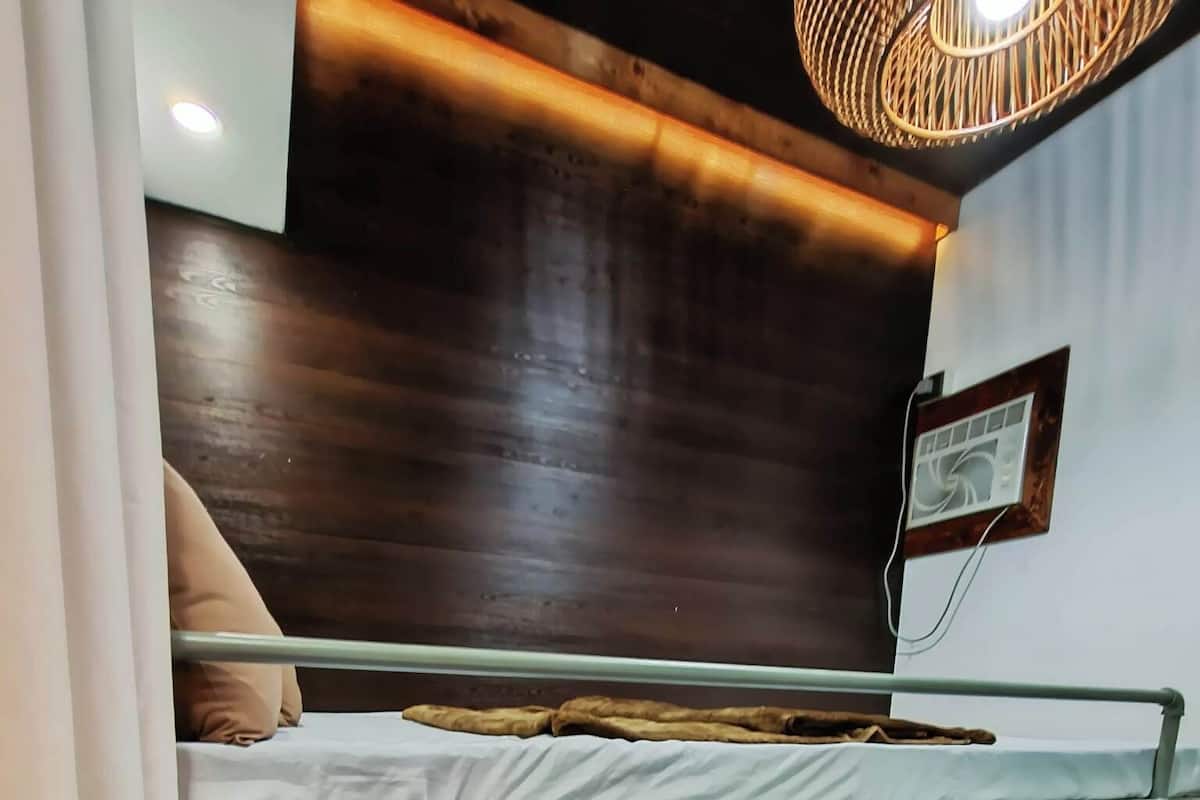 Uma cama beliche com cabeceira de madeira, uma pequena prateleira com um porta-retrato e uma luminária fixada na parede.