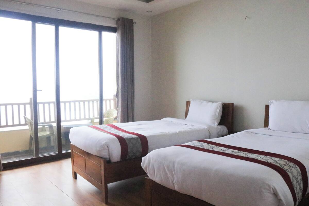 A hotel room with two beds, a balcony with a view, and a sliding glass door.
