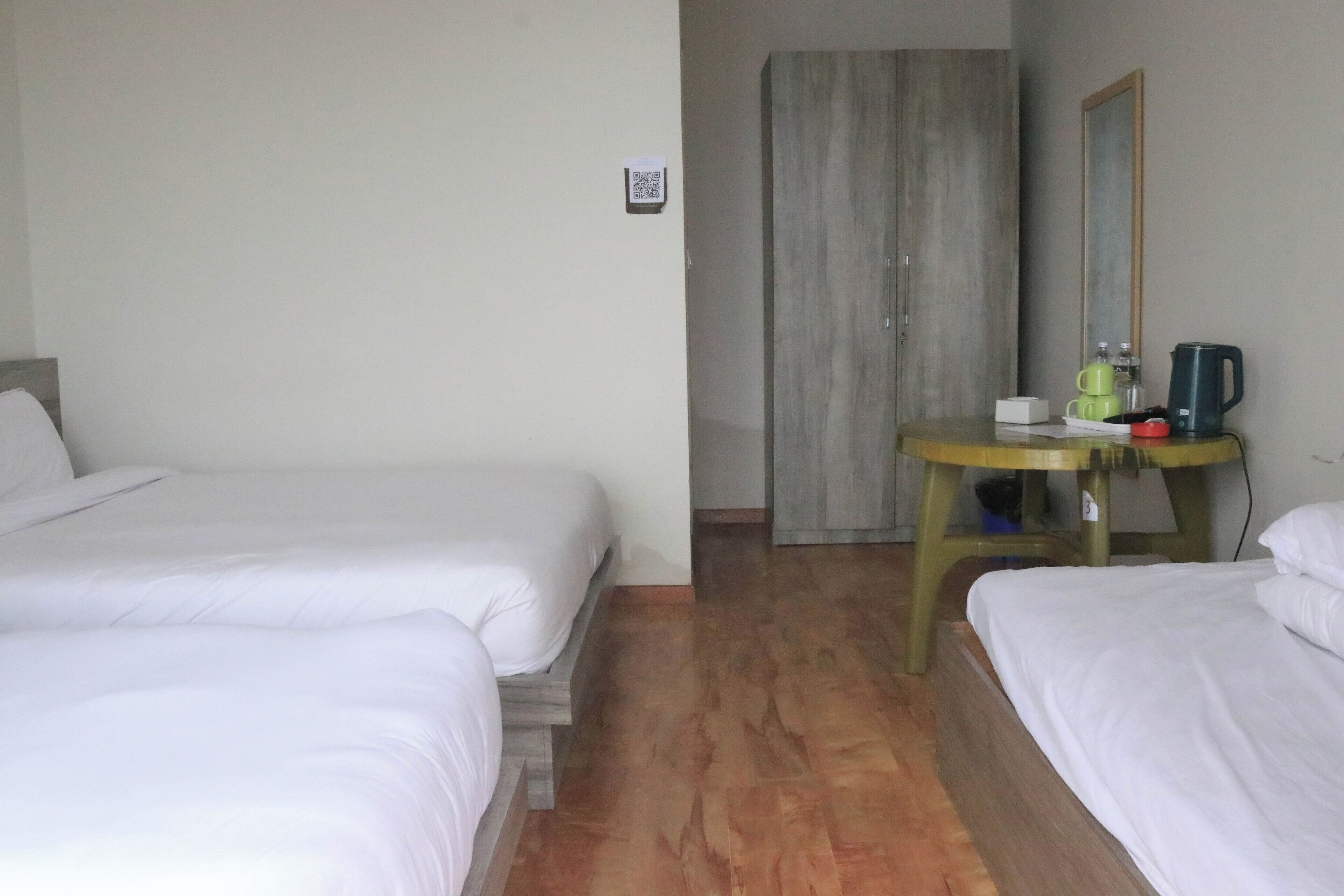 Habitación de hotel con dos camas individuales, piso de madera, una mesita con hervidor y un armario.