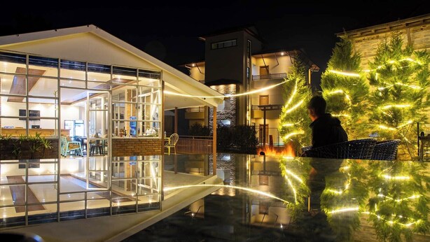 A modern building with a glass facade, outdoor seating, and a well-lit patio area. - Indrasthan himalaya Resort  (Chandragiri)