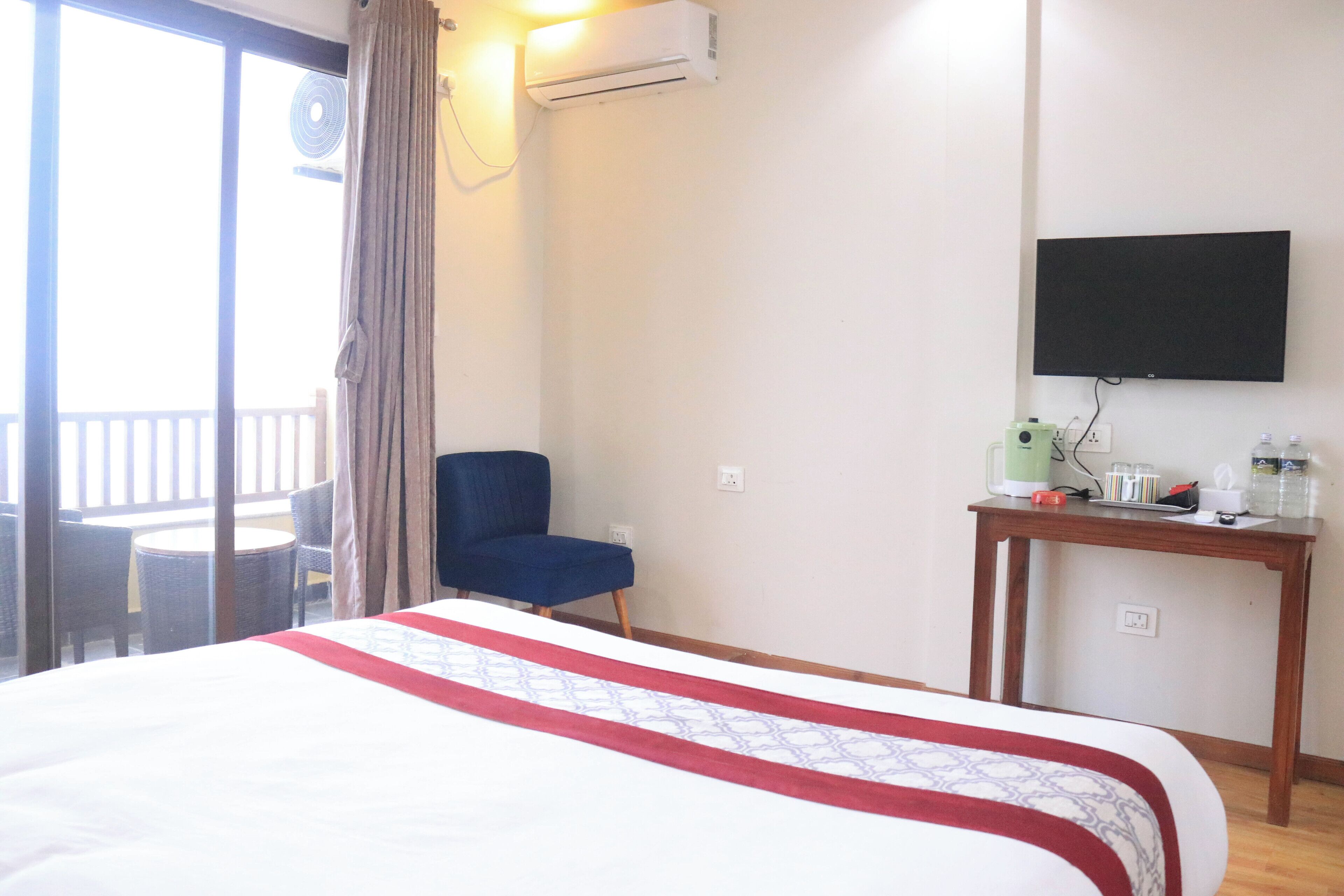 A hotel room with a bed, a chair, a table with a TV, and an air conditioning unit.