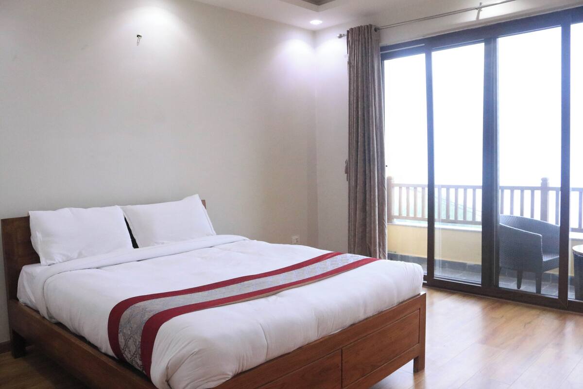 A bedroom with a wooden bed, white bedding, and a view of a balcony with a chair.