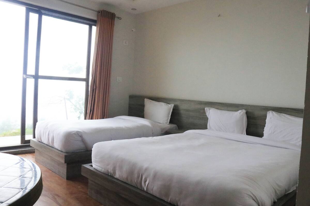 A hotel room with two beds, a large window, and a round table.