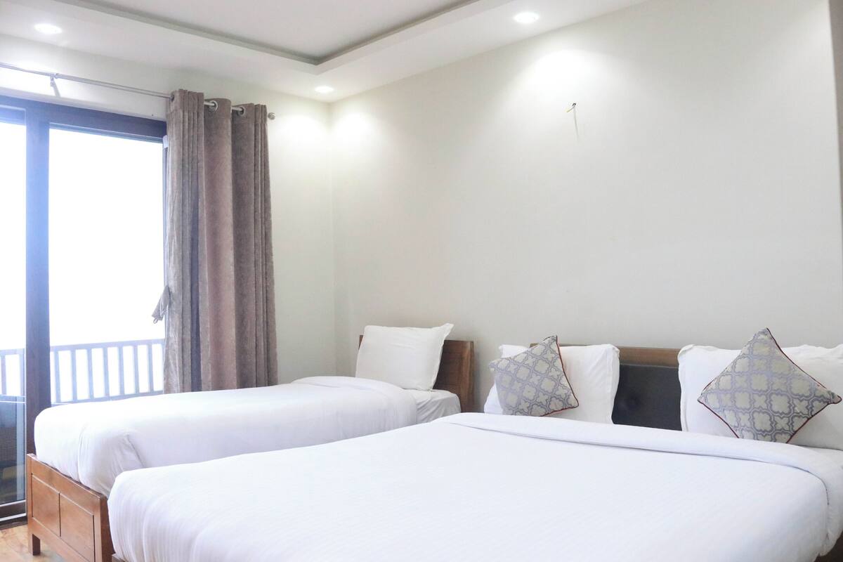 A hotel room with two single beds, a large window with curtains, and a balcony.