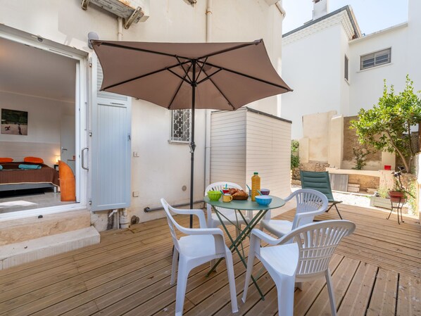 A wooden deck with a table and chairs, a large umbrella, and a breakfast setup with croissants and drinks.