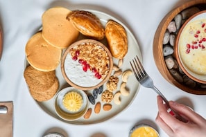 Un plat d'esmorzar amb crepes, iogurt, granola, fruits secs i un bol petit de mantega.