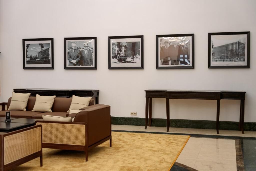 A room with a brown sofa, a small table, and a large framed picture on the wall.