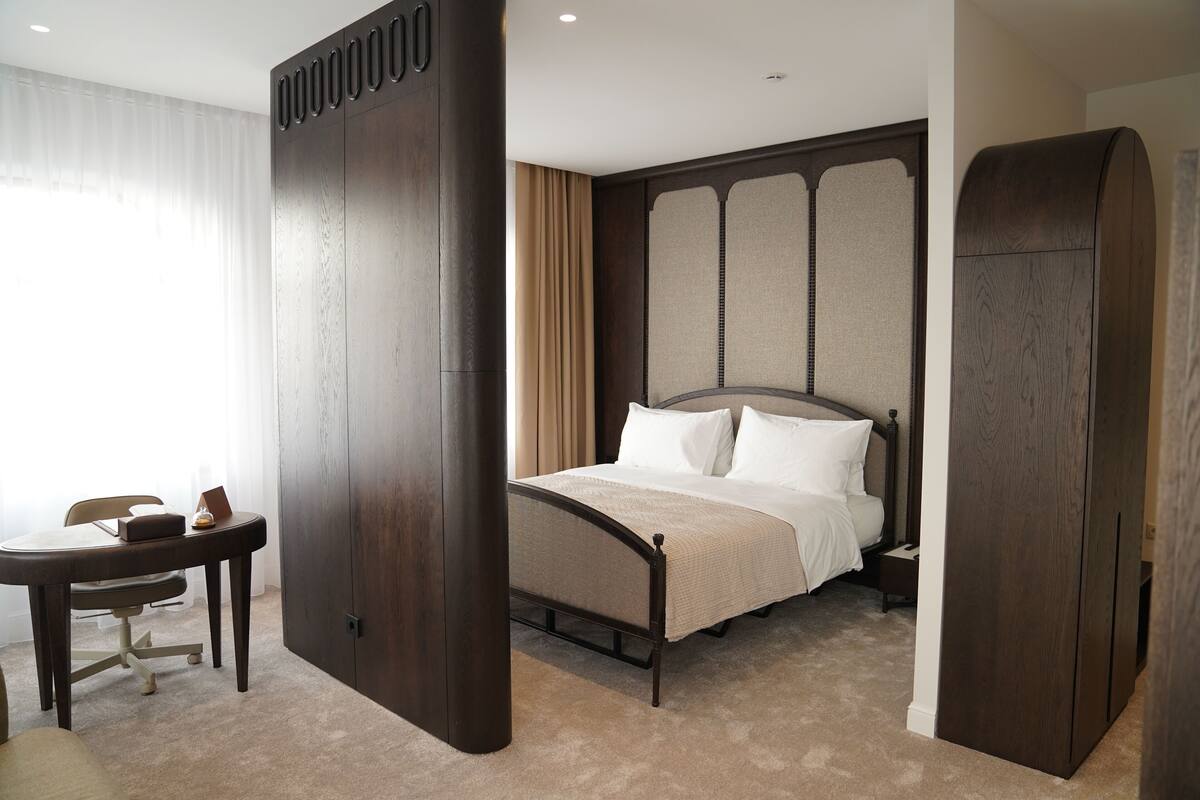 A hotel room with a large bed, a desk, and a wardrobe.