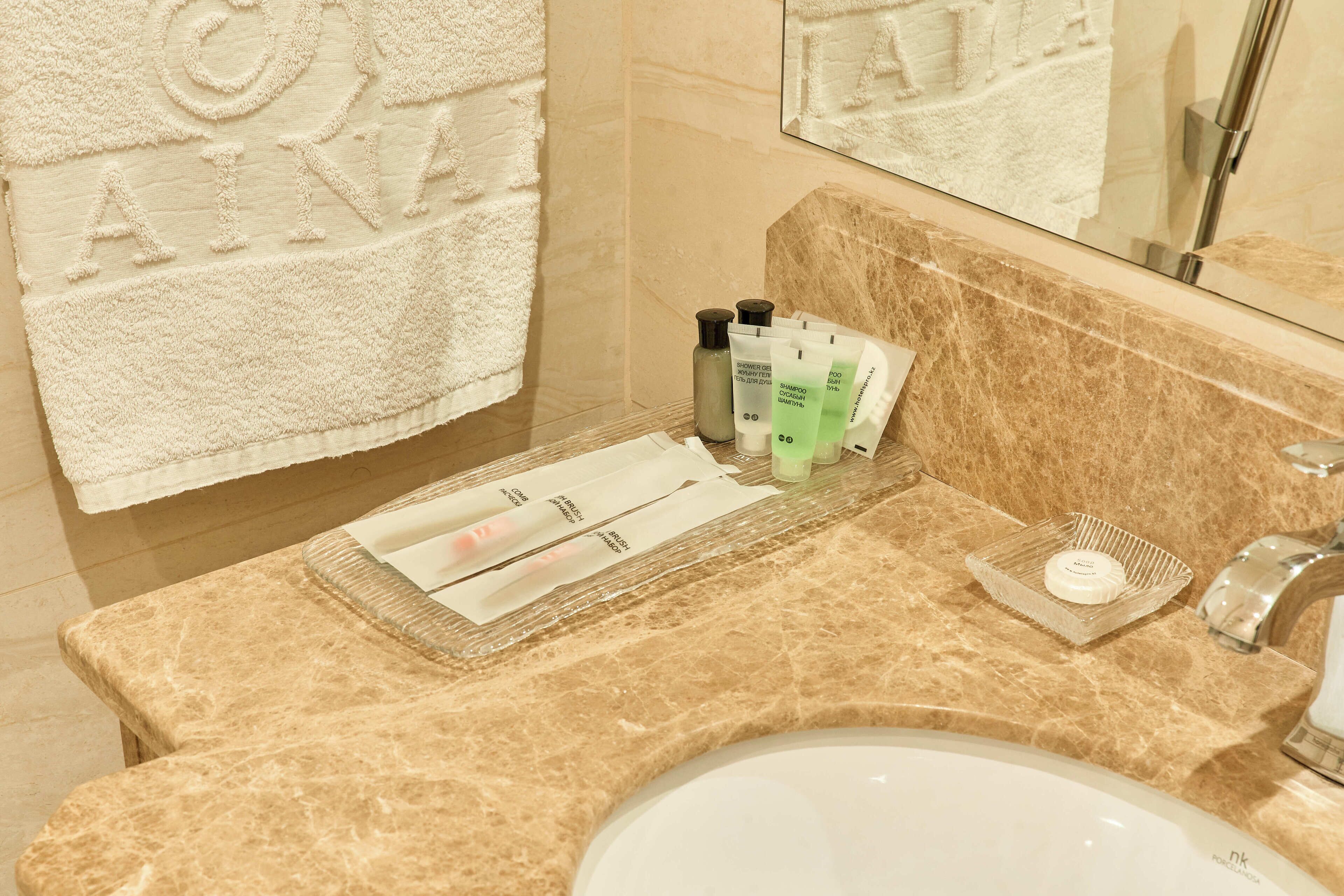 A bathroom with a beige marble countertop, a sink, and toiletries including a bottle, tubes, and a soap dish.