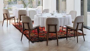 Een eetgedeelte met ronde tafels, stoelen en uitzicht door grote ramen.
