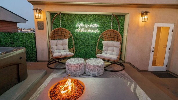 An outdoor seating area with two wicker chairs, a fire pit, and a neon sign stating "life is better at the beach". - 4 Br, Roof Deck, Hot Tub, Steps to Beach & Dining (Newport Beach)