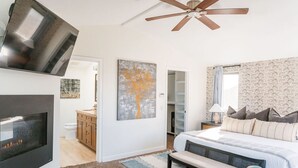 A modern bedroom with a fireplace, a ceiling fan, a bed with pillows, a bench, and a wardrobe. - 4 Br, Roof Deck, Hot Tub, Steps to Beach & Dining (Newport Beach)