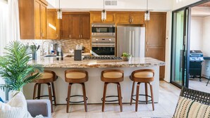 A modern kitchen with wooden cabinets, stainless steel appliances, and a central island with bar stools. - 4 Br, Roof Deck, Hot Tub, Steps to Beach & Dining (Newport Beach)