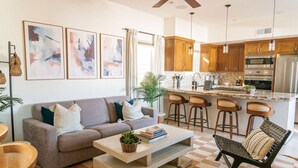 A modern living room with a sofa, coffee table, and a dining area with bar stools. - 4 Br, Roof Deck, Hot Tub, Steps to Beach & Dining (Newport Beach)