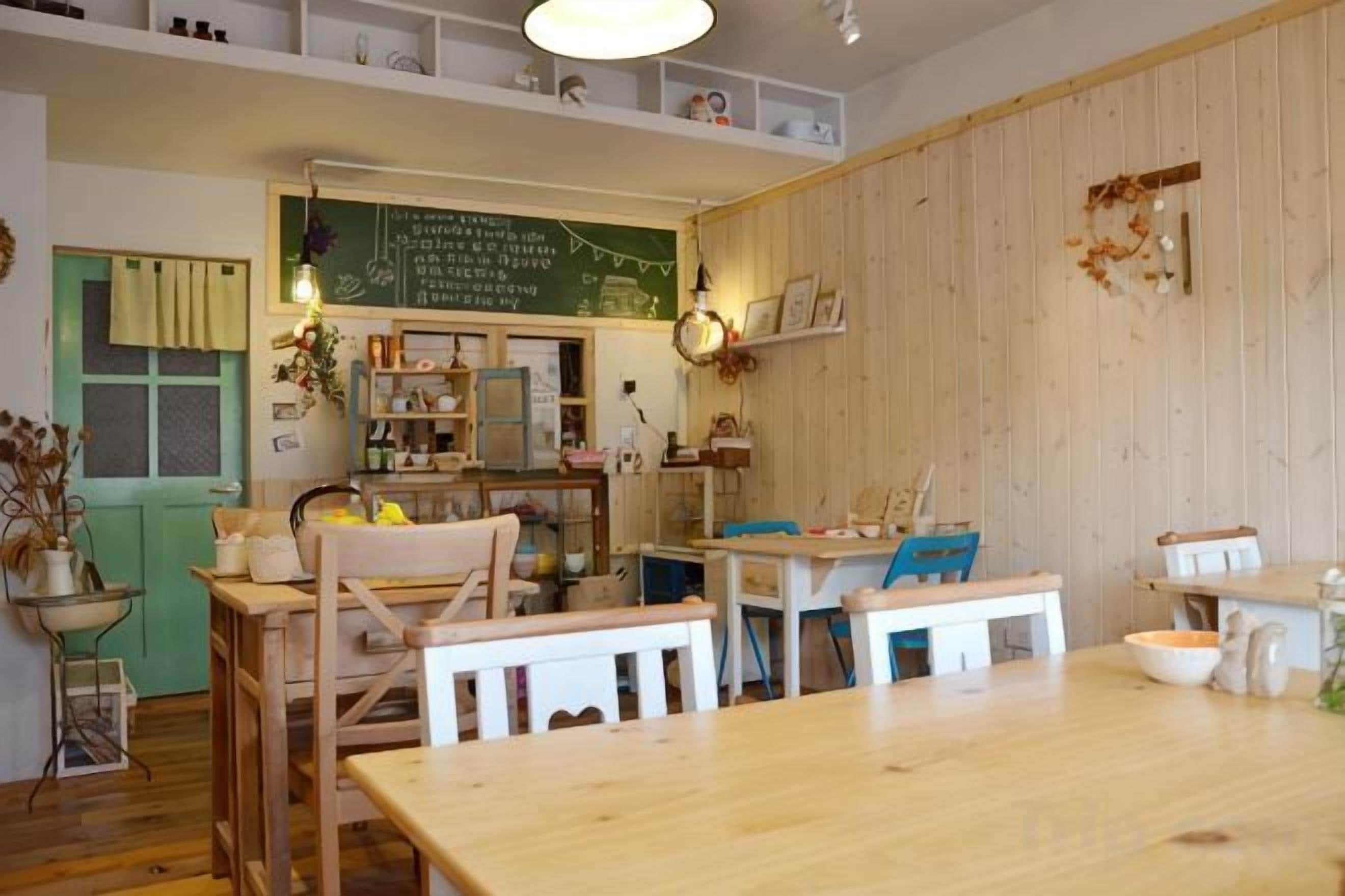 Ein gemütlicher Raum mit einem Holztisch, Stühlen, einer Kreidetafel und Regalen mit verschiedenen Gegenständen.