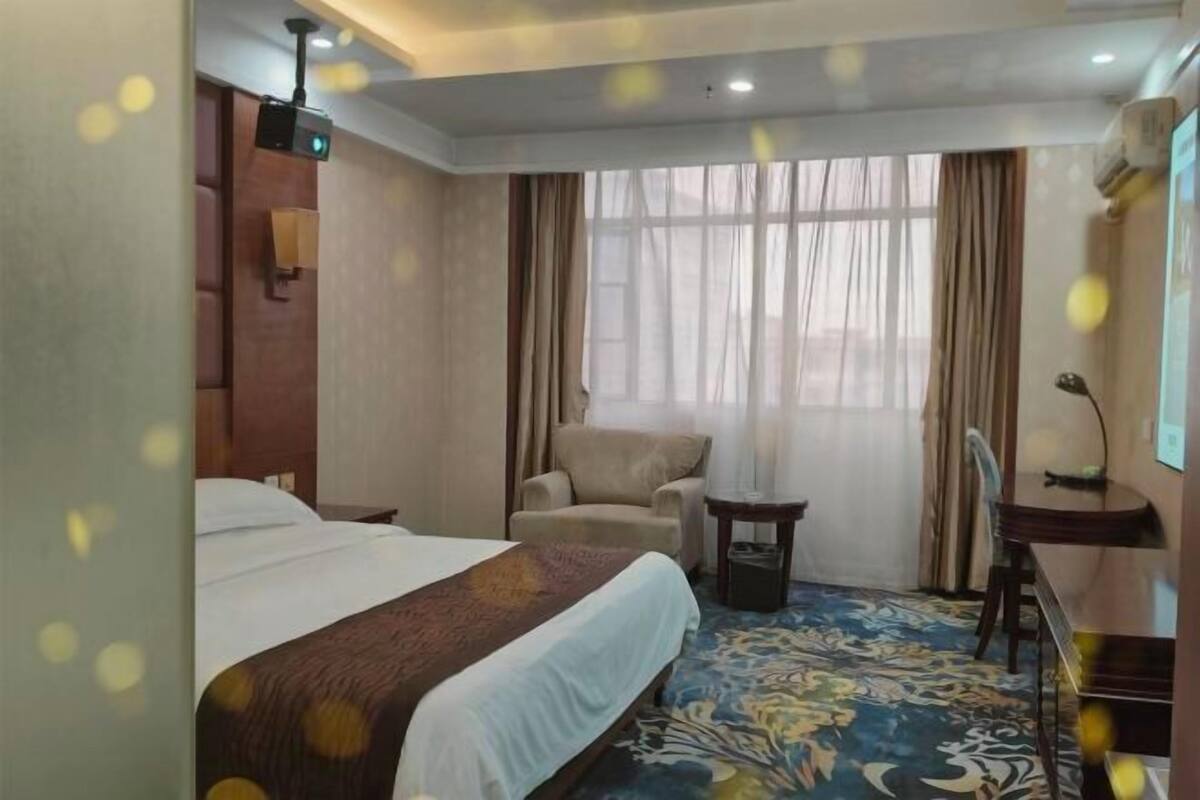 A hotel room with a bed, a desk, a chair, a small table, and a window with curtains.