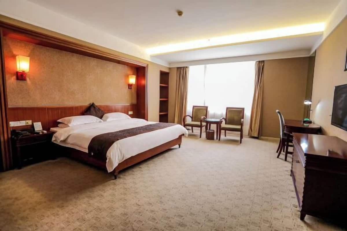 A hotel room with a large bed, bedside tables, a desk, chairs, and a TV.