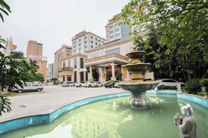 A hotel with a fountain in the courtyard, surrounded by greenery and parked cars. - Xinghe Hotel(Dongguan Humen road east) (Dongguan)
