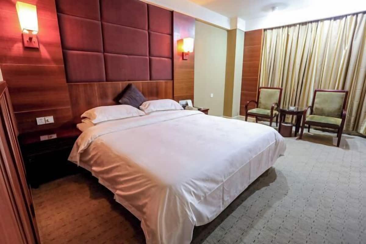 A hotel room with a large bed, two bedside tables, a chair, and a curtain.