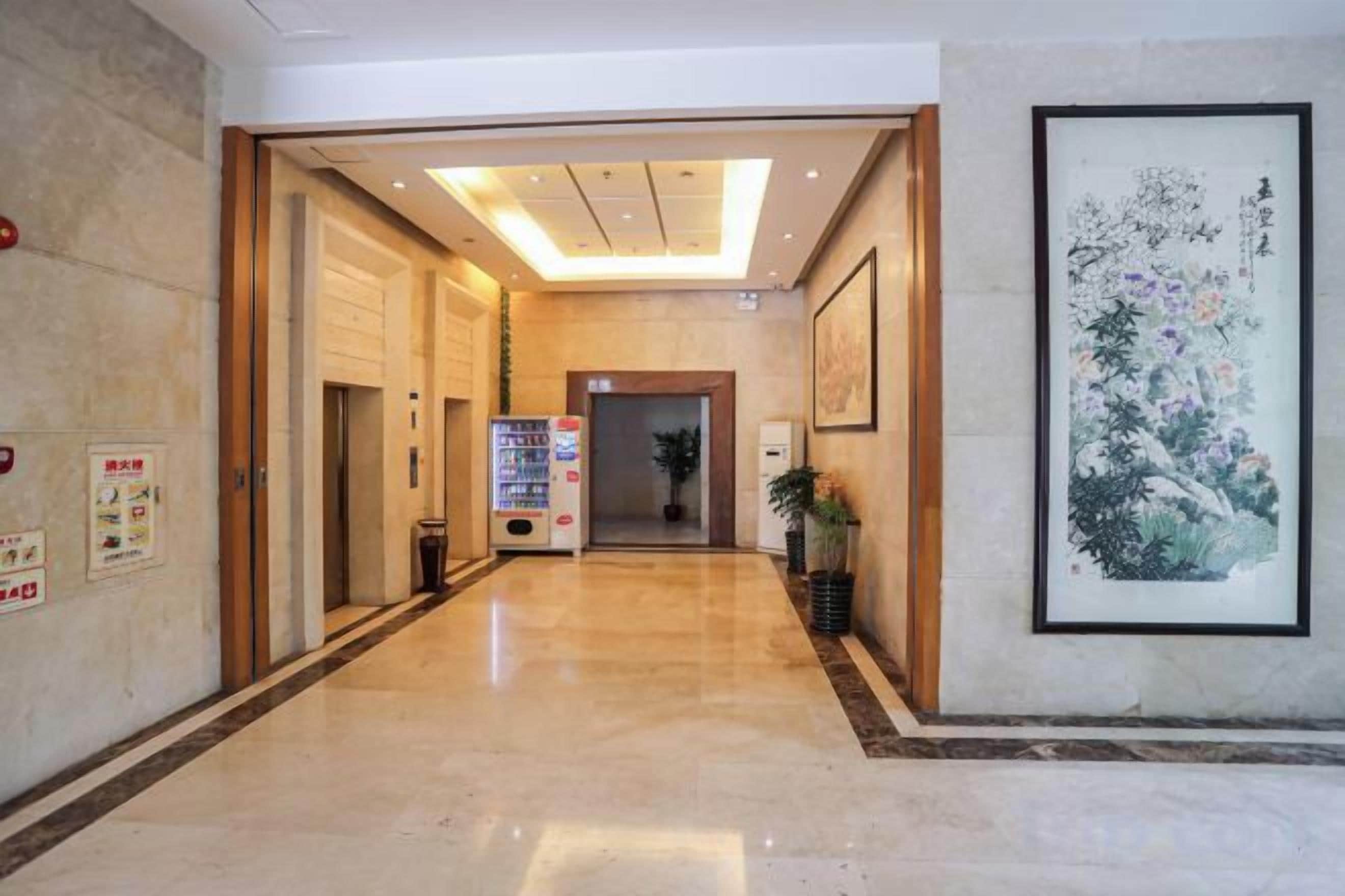 A hotel lobby with a marble floor, wooden doors, a vending machine, and a framed artwork on the wall.