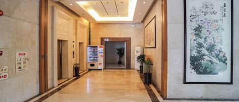 A hotel lobby with a marble floor, wooden doors, a vending machine, and a framed artwork on the wall.
