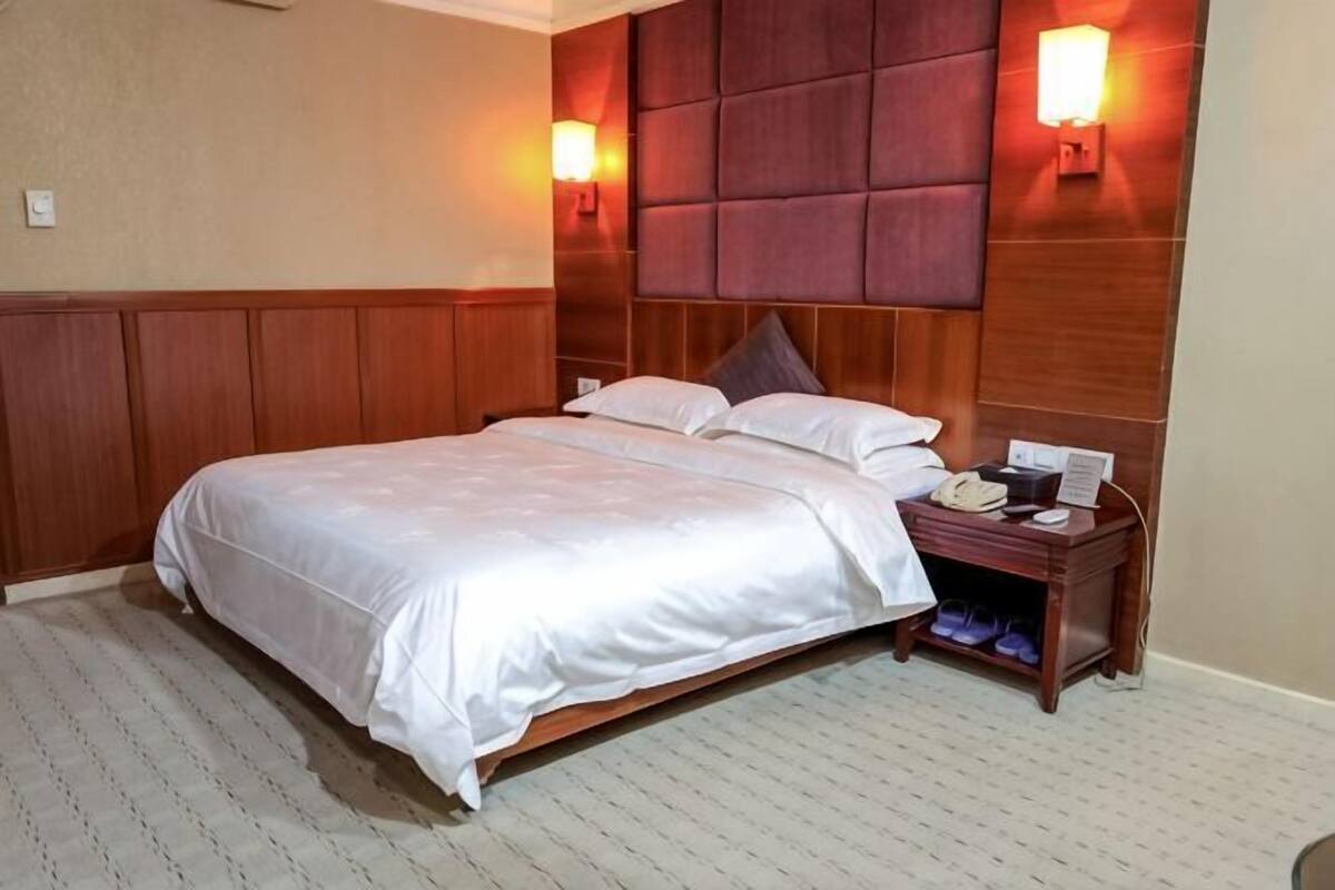 A hotel room with a large bed, two bedside lamps, a wooden headboard, and a nightstand with a phone and a lamp.