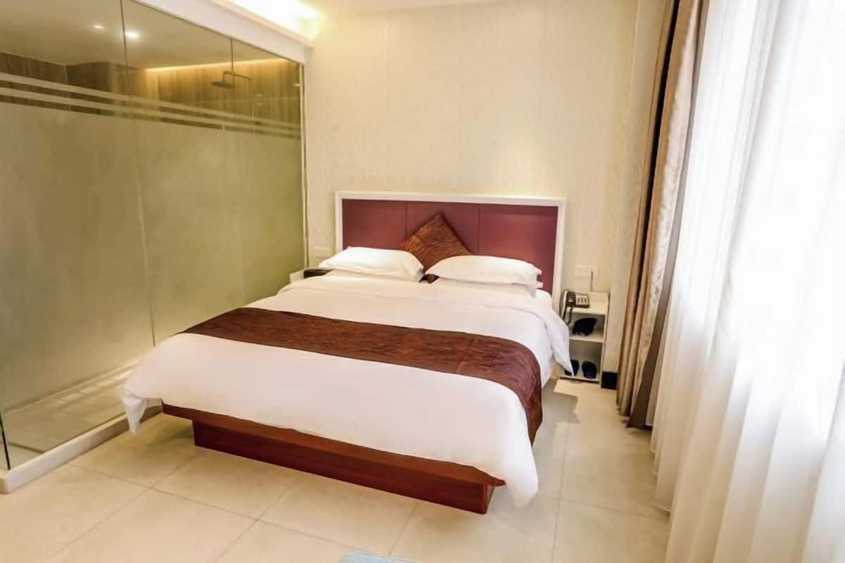 A hotel room with a bed, a glass shower enclosure, and a bedside table.