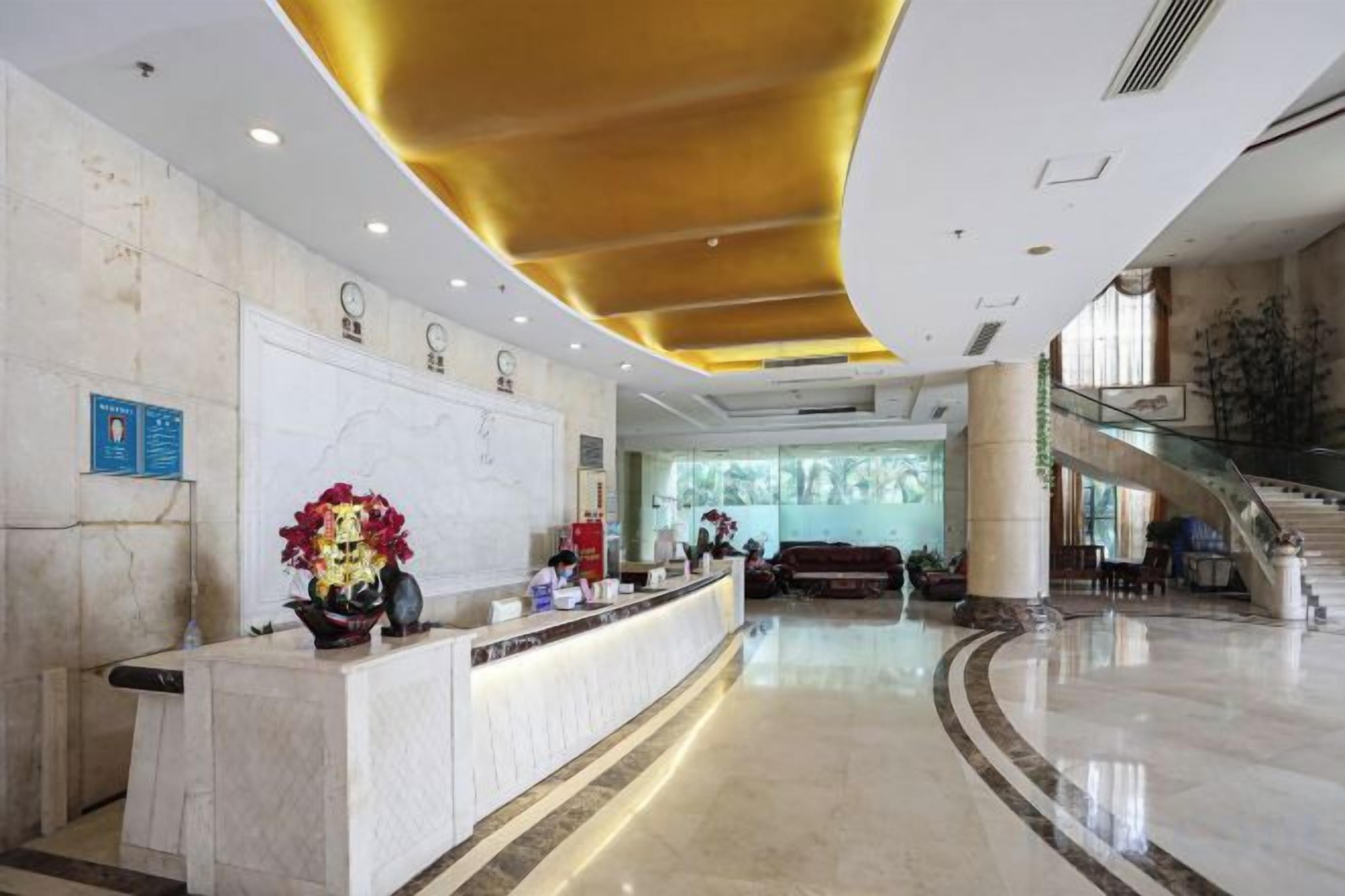 A hotel lobby with a reception desk, a staircase, and a large window.