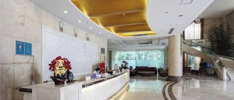 A hotel lobby with a reception desk, a staircase, and a large window.