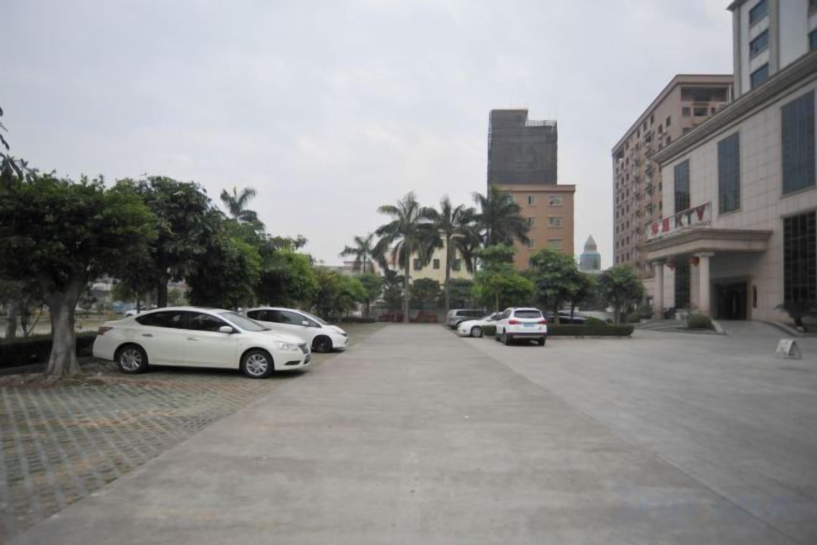 A parking lot with several cars, trees, and buildings in the background.