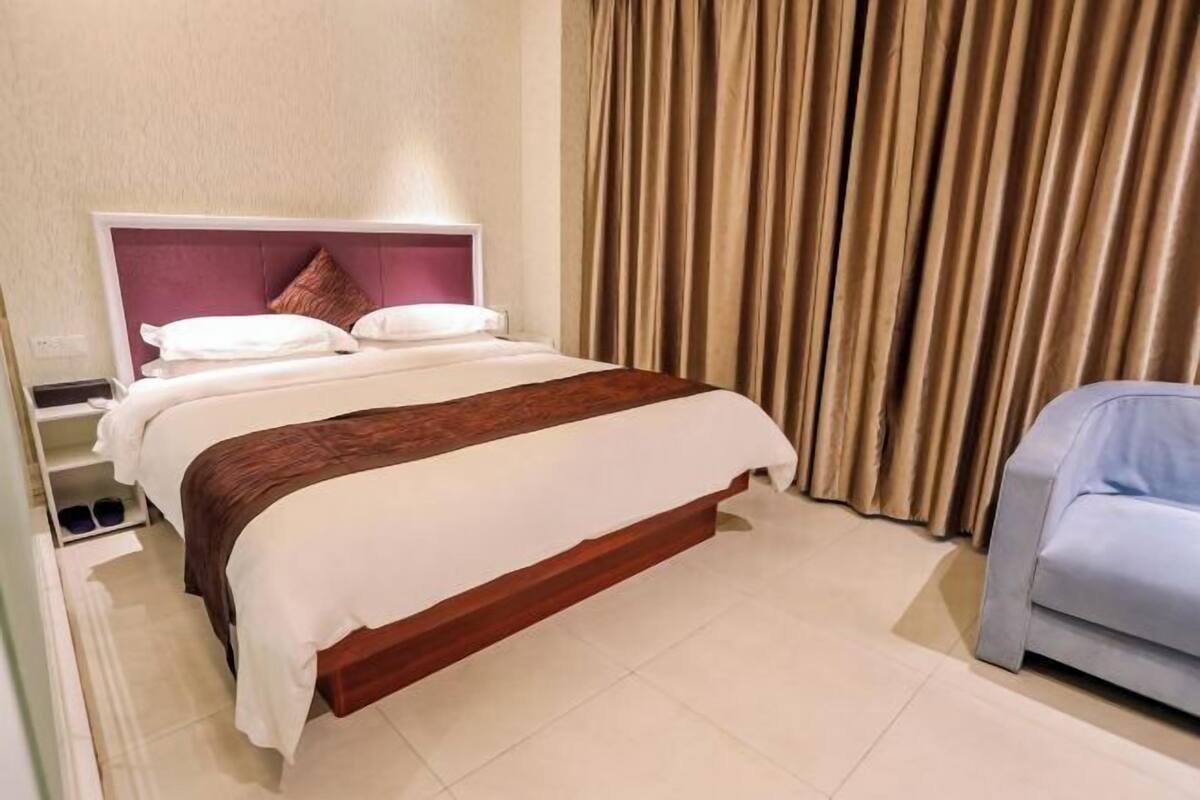 A hotel room with a bed, a nightstand, a chair, and a curtain.