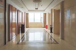 A hotel corridor with a polished floor, a trash bin, and a potted plant. - Xinghe Hotel(Dongguan Humen road east) (Dongguan)