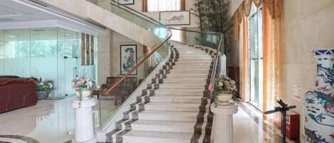 A grand staircase with marble steps, glass railings, and decorative columns.